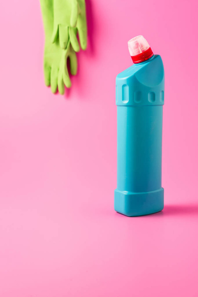 Nahaufnahme von Reinigungsflüssigkeit und Gummihandschuhen dahinter, rosa Hintergrund  - Foto, Bild