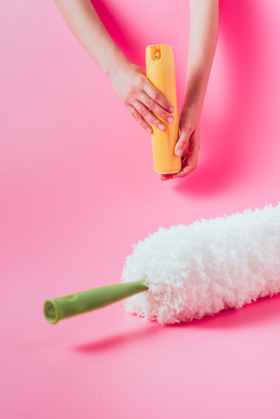 partial view of female cleaner holding spray can near white duster, pink background  - Foto, Imagen