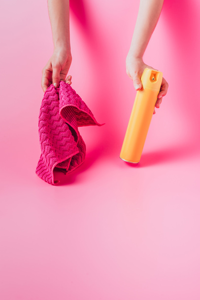 cropped image of woman holding spray can and rag, pink background  - Zdjęcie, obraz