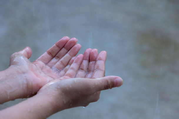 Nahaufnahme einer Frau, die ihre Hand in den Regen steckt und Regentropfen auffängt, Wasserkonzept. - Foto, Bild