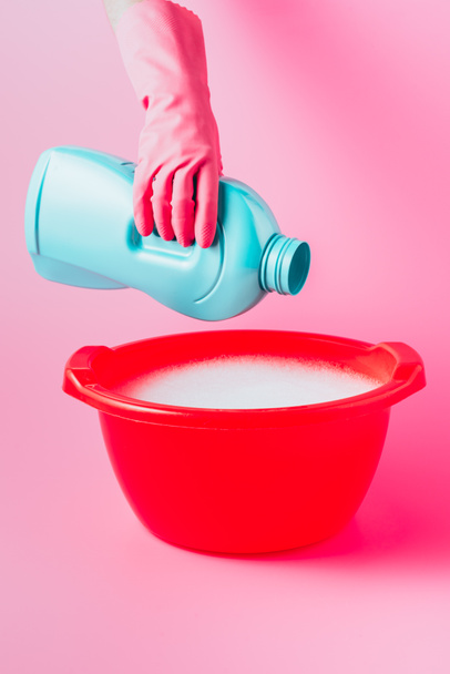 partial view of female cleaner pouring laundry liquid in plastic basin with foam, pink background - Foto, Bild