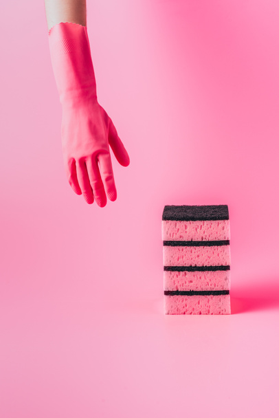 image recadrée de femme nettoyeuse main dans un gant en caoutchouc près de pile d'éponges de lavage, fond rose
 - Photo, image