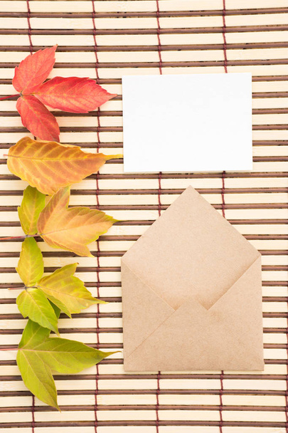 Krásné barevné zelené, červené a žluté podzimní javorové listy a obálku s prázdnou zprávou na hnědé pozadí - Fotografie, Obrázek