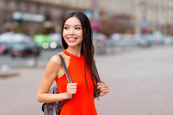 Portrait of attractive asian girl in red dress standing in half-turned close up photo against a blurred background of cityscape meeting with friend - Fotoğraf, Görsel