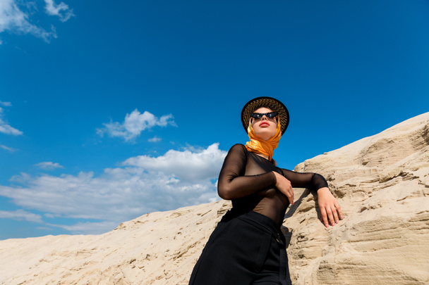 bottom view of elegant woman posing near sand dune with blue sky on background - Zdjęcie, obraz