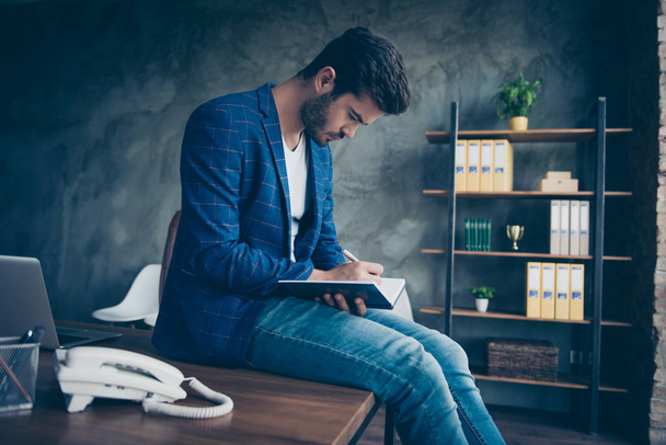 Attractive handsome young brunet bearded serious executive worker man in office workstation workplace, sitting on table, writing notes in paper note book, diary, making strategy plans - Valokuva, kuva