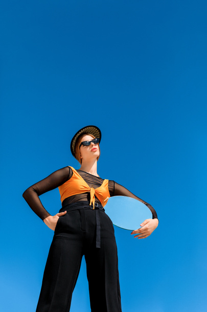 bottom view of fashionable girl posing with round mirror, blue sky on background - Photo, Image