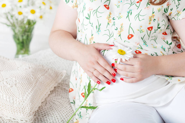 Closeup of pregnant woman holding flower and touching her belly - Foto, imagen