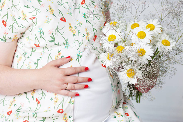 Closeup of pregnant woman holding flower and touching her belly - Φωτογραφία, εικόνα