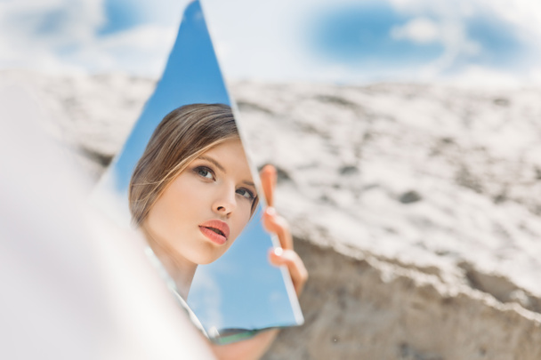 charming girl holding piece of mirror and looking on her reflection - Фото, изображение