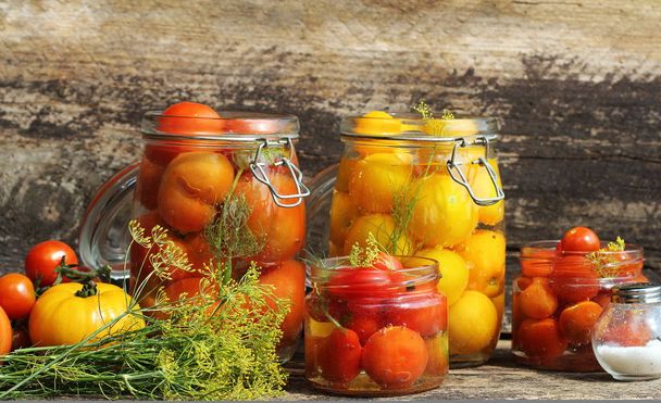 Pickled tomato in jars on wooden table . Tomatoes fermented process glass jars variety - red yellow, orange colors - Photo, Image