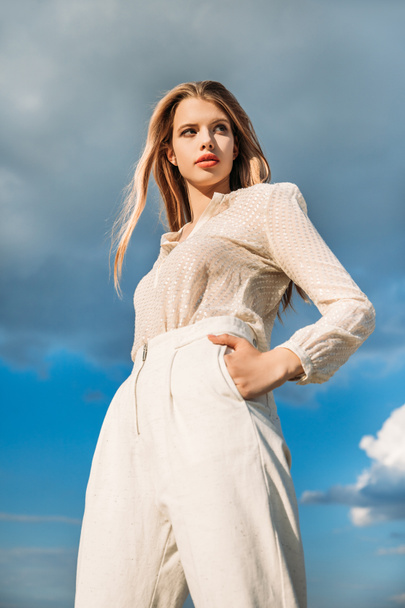 bottom view of elegant fashionable model posing in white stylish clothes with cloudy sky on background - Photo, Image