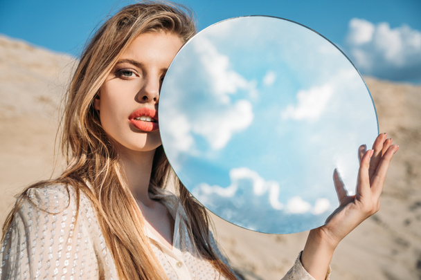 ελκυστικό μοντέλο κομψό κρατά στρογγυλή καθρέφτη με αντανάκλαση του συννεφιασμένο ουρανό - Φωτογραφία, εικόνα