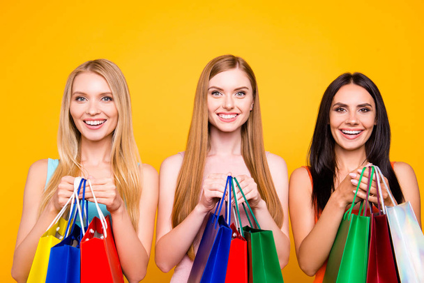 Boutique center mall showroom package commerce black friday concept. Portrait of charming pretty trio holding many colorful bags in hands enjoying seasonal sales isolated on vivid yellow background - Photo, Image