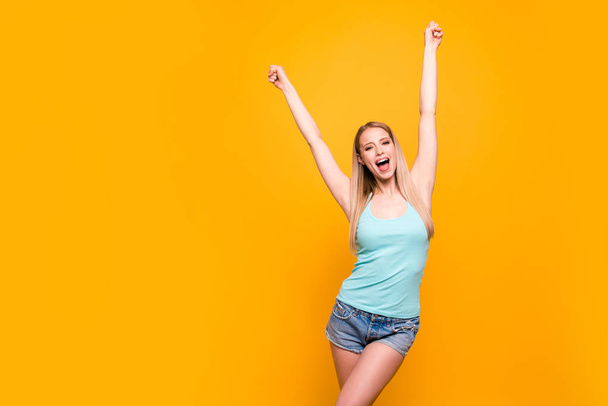 VICTORY! Charming young model with long blond hair raises her fists up and triumphantly screams "goal" isolated on shine yellow background with copy space for text - Foto, immagini