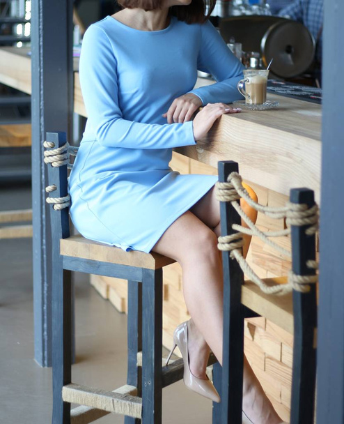 girl in blue dress sits at a bar counter and drinks coffee.communicates with the barman, a cup of coffee stands on the bar - Fotó, kép