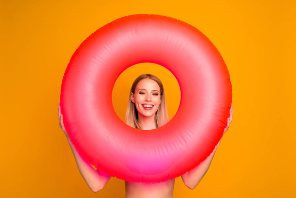 Travel and daydream concept. Positive blond girl look through pink rubber rings enjoying rest isolated on bright yellow background - Valokuva, kuva