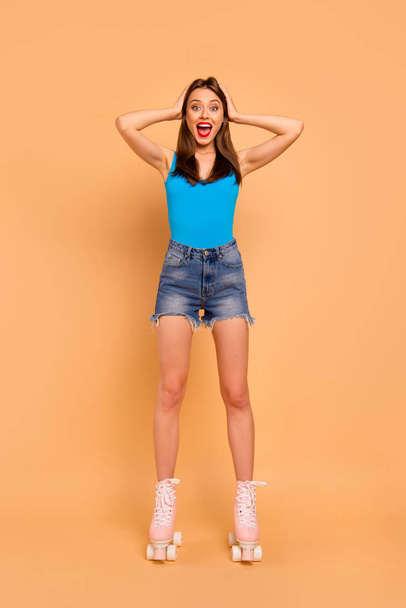 Full-legs vertical portrait of shocked brunette girl with hands behind her head with wide open mouth in red bright lipstick isolated on pastel peach background - Fotó, kép