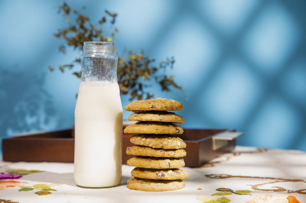 Složení s cookie hromadu a mléko láhev v tabulce. Ranní slunce v modré pozadí s texturou. - Fotografie, Obrázek