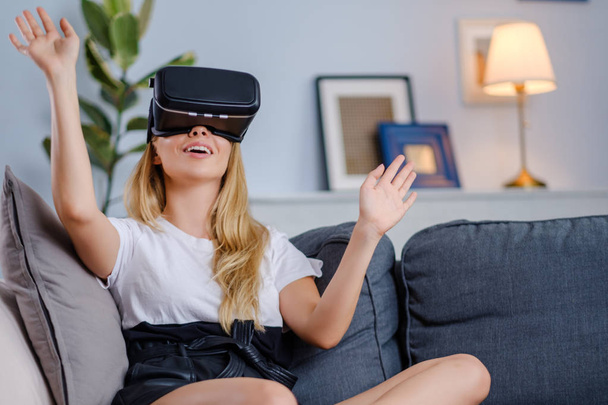 Привлекательная молодая женщина в наушниках VR жестикулирует и улыбается
 - Фото, изображение