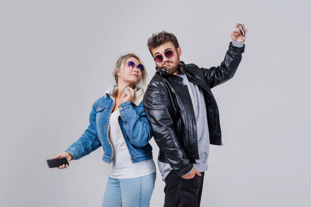 Portrait of a young couple enjoying music and make selfie over grey background - Foto, imagen