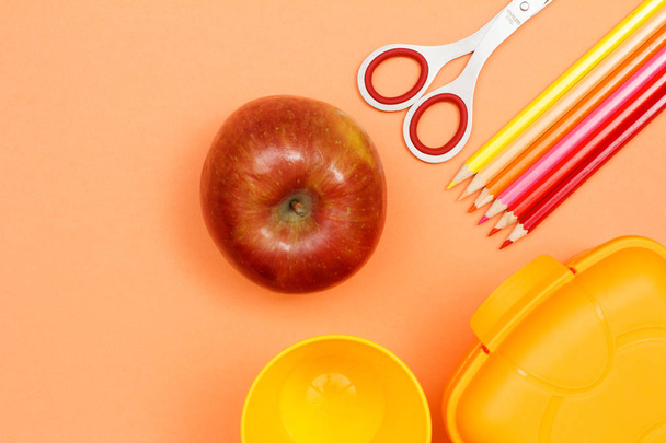 Des fournitures scolaires. Pomme, ciseaux, feutres, crayons de couleur et boîte à lunch sur fond rose. Vue supérieure avec espace de copie. Retour à l'école. Couleurs pastel
 - Photo, image