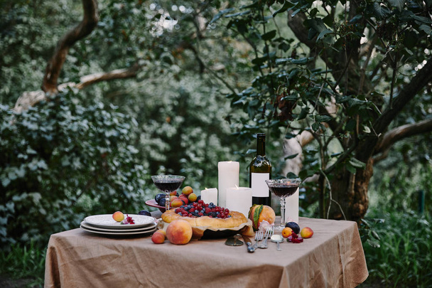 tasty appetizing berries pie, red wine and candles on table in garden - Photo, Image