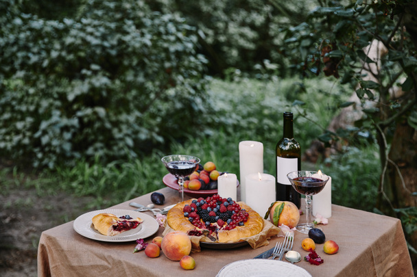 tasty appetizing berries pie and wine on table in garden - Фото, изображение