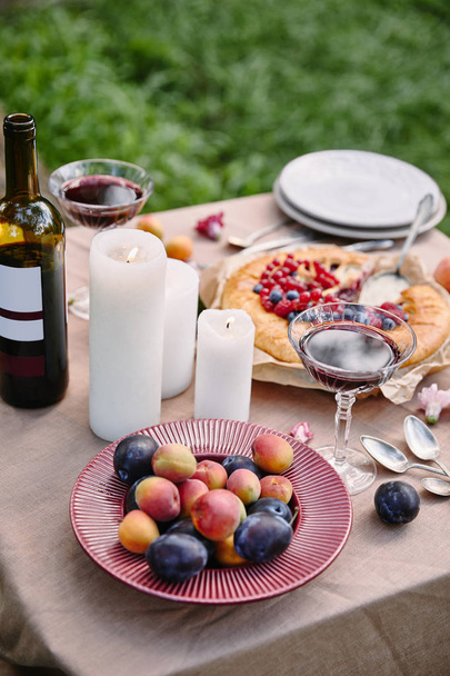 fruits, candles and wine bottle on table in garden - Valokuva, kuva