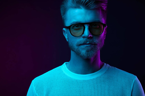 Neon light studio portrait of serious man model with mustaches and beard in sunglasses and white t-shirt  - Foto, Bild