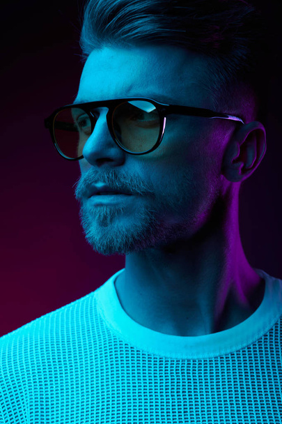 Neon luz estúdio retrato de homem sério modelo com bigodes e barba em óculos de sol e t-shirt branca
  - Foto, Imagem