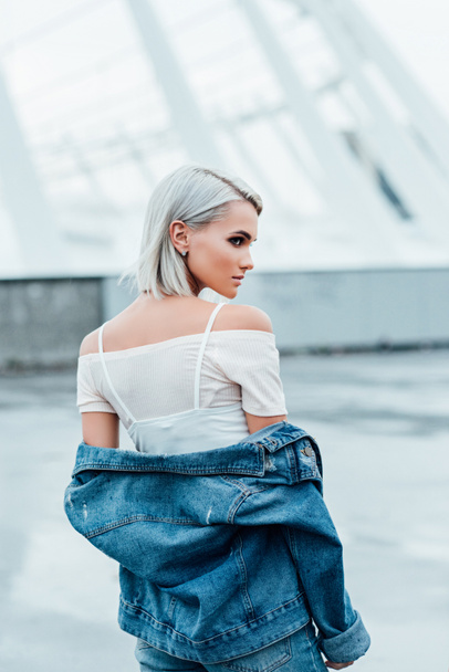 rear view of stylish young woman with bleached hair and in denim jacket on street - Photo, image