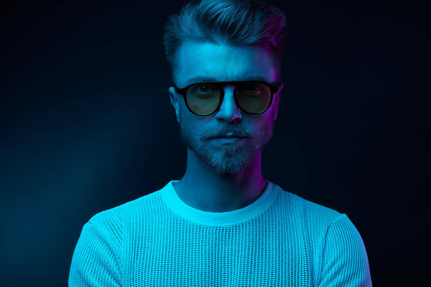 Neon light portrait of serious man model with mustaches and beard in sunglasses and white t-shirt  - Photo, image