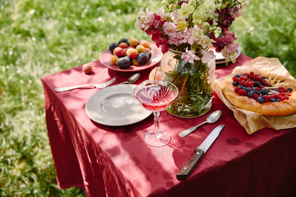 vinho, torta de bagas e buquê de flores na mesa no jardim
 - Foto, Imagem