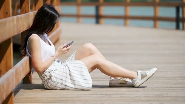 Aranyos nő olvas szöveges üzenetet a mobiltelefon, miközben ül a parkban. - Felvétel, videó