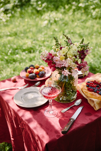 wineglass and bouquet of flowers on table in garden - Zdjęcie, obraz
