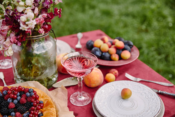 berries pie, wineglass and bouquet of flowers on table in garden - Fotó, kép