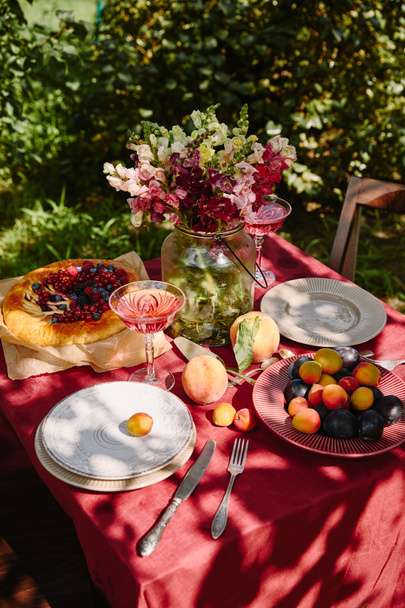 bouquet of flowers, fruits and appetizing pie on table in garden - Фото, изображение