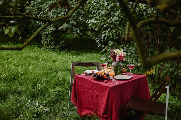 bouquet of flowers, wineglasses and fruits on table in garden - Foto, Imagem