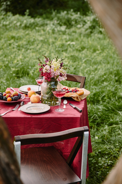 μπουκέτο με λουλούδια σε γυάλινο βάζο και φρούτα στο τραπέζι στον κήπο - Φωτογραφία, εικόνα