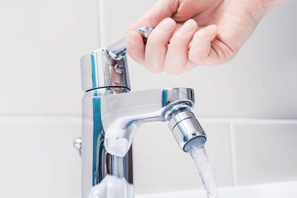 Mano femminile sulla maniglia di un rubinetto cromato con acqua corrente
 - Foto, immagini