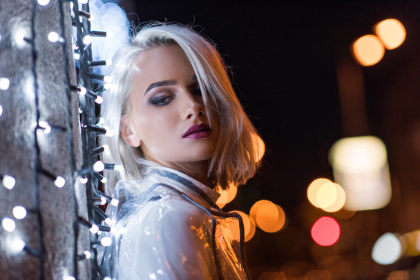 bella giovane donna appoggiata al muro con ghirlanda bianca sulla strada della città di notte
 - Foto, immagini