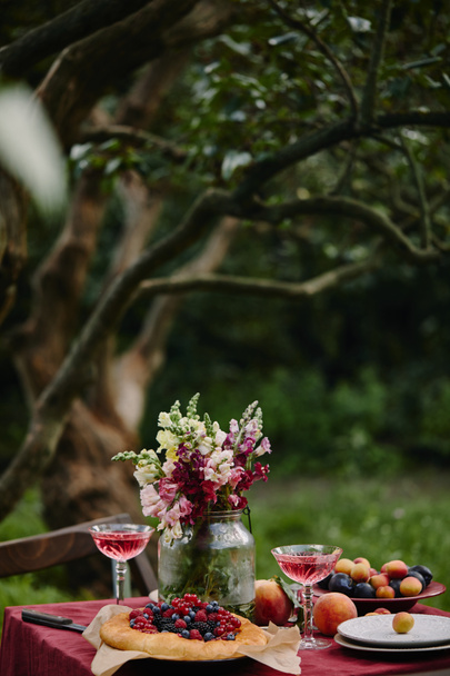 bouquet of flowers in glass jar, pie and wineglasses on table in garden - Photo, Image