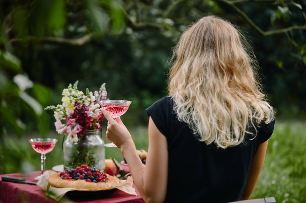 задний вид женщины, держащей бокал вина за столом в саду
 - Фото, изображение