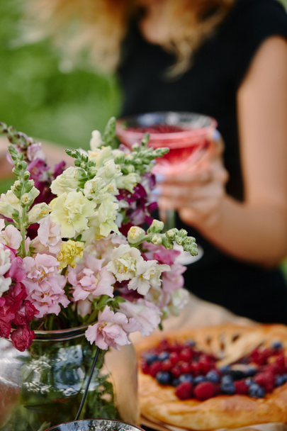 前景の花の庭のテーブルでワインのガラスを保持している女性のトリミングされた画像 - 写真・画像