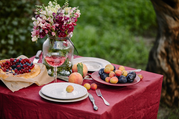 glasses of wine, berries pie and fruits on table in garden - Fotó, kép