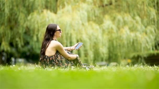 Мила жінка читає текстове повідомлення на мобільному телефоні, сидячи в парку
. - Кадри, відео