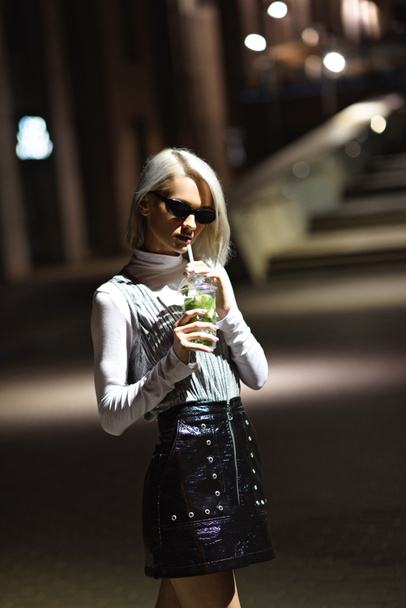 beautiful young woman with mojito in plastic cup on dark street - Foto, afbeelding