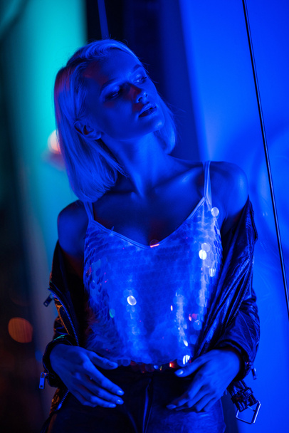 beautiful young woman in glossy tank top on street at night under blue light - Photo, Image