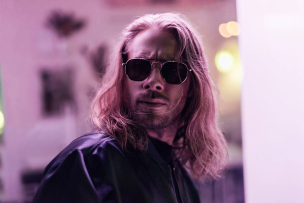 close-up portrait of handsome young man in leather jacket and sunglasses on street at night under pink light - Фото, зображення